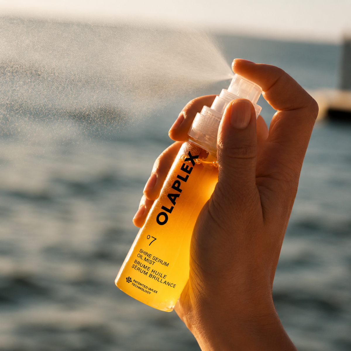 Hand holding a bottle of Olaplex Shave Serum with a blurred water background