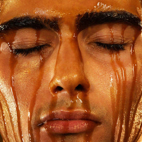 Man's face with eyes closed coated in amber liquid