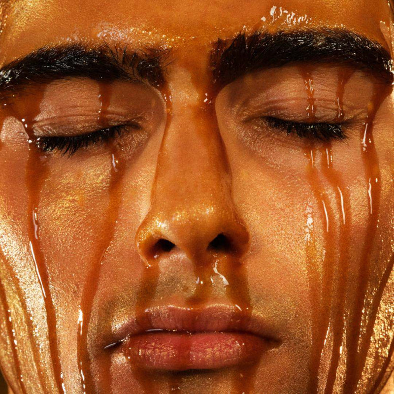 Close-up of a man's face with closed eyes and amber liquid dripping down the cheeks and over the eyebrows.
