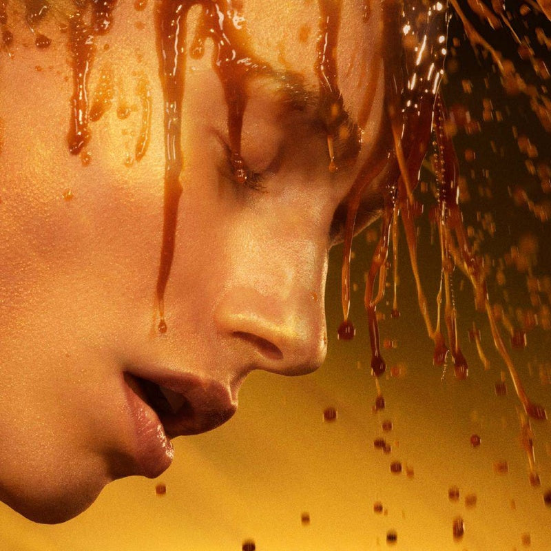 Woman's face on yellow/brown background with amber liquid pouring from above.